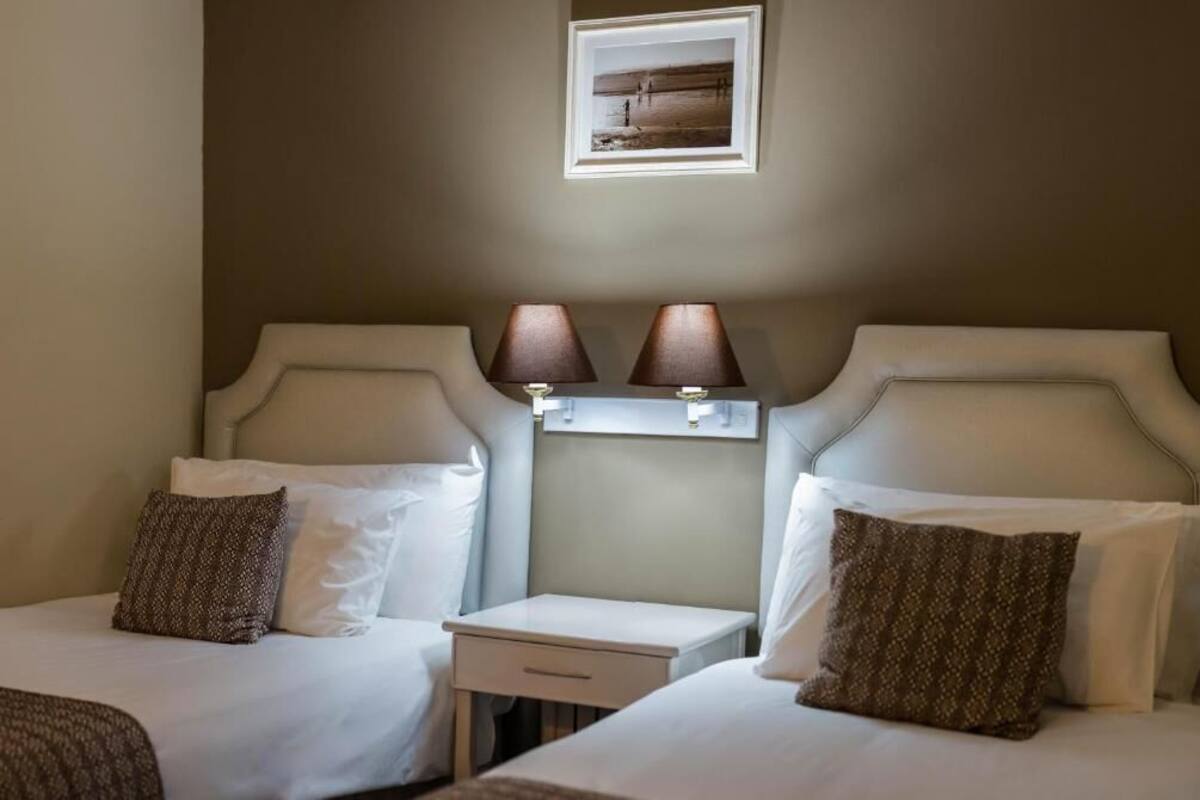 Een hotelkamer met twee eenpersoonsbedden, een klein nachtkastje met lampen en een lijst met een afbeelding aan de muur.