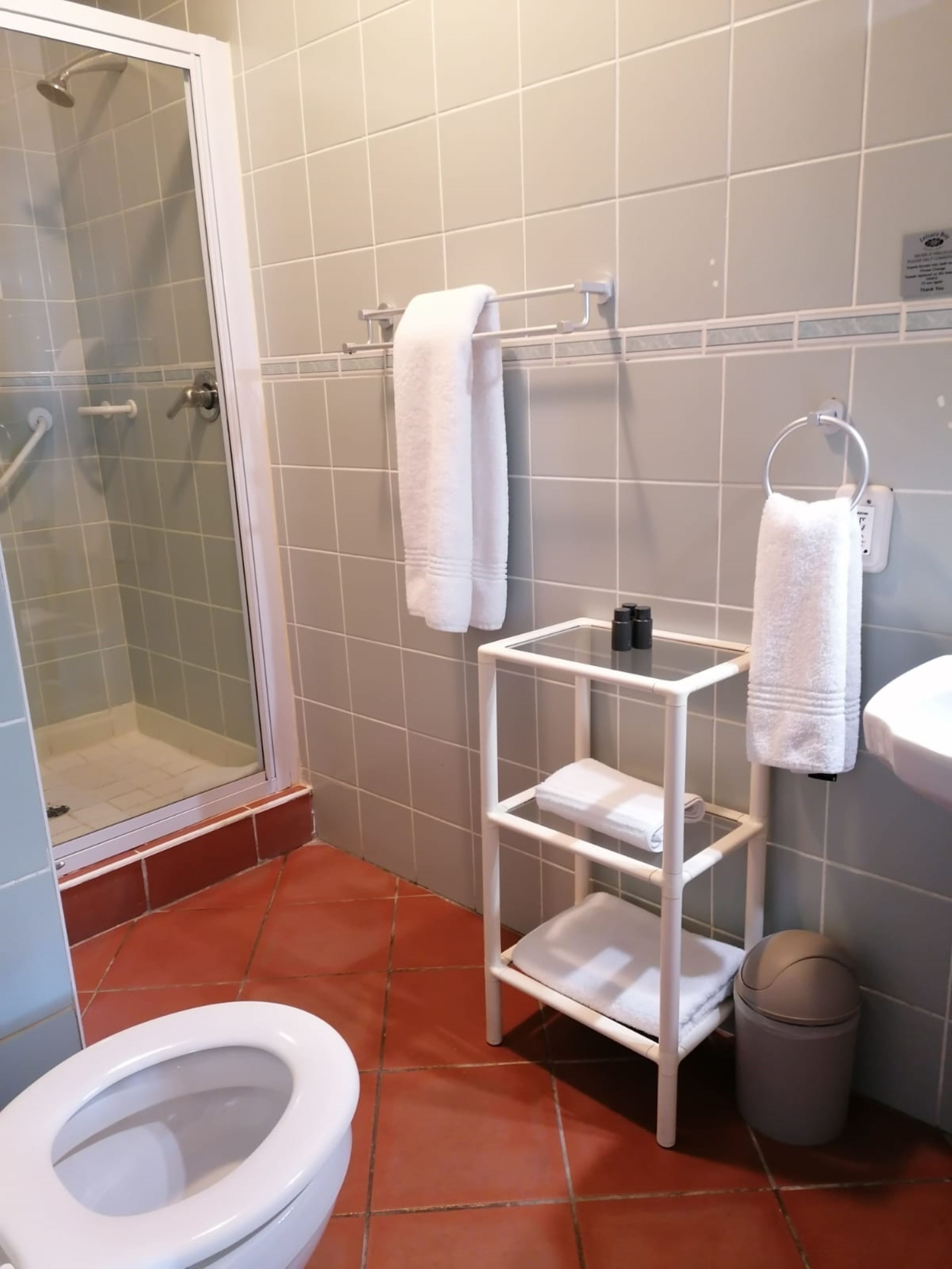 A bathroom with a shower, toilet, and a white shelf unit with towels.
