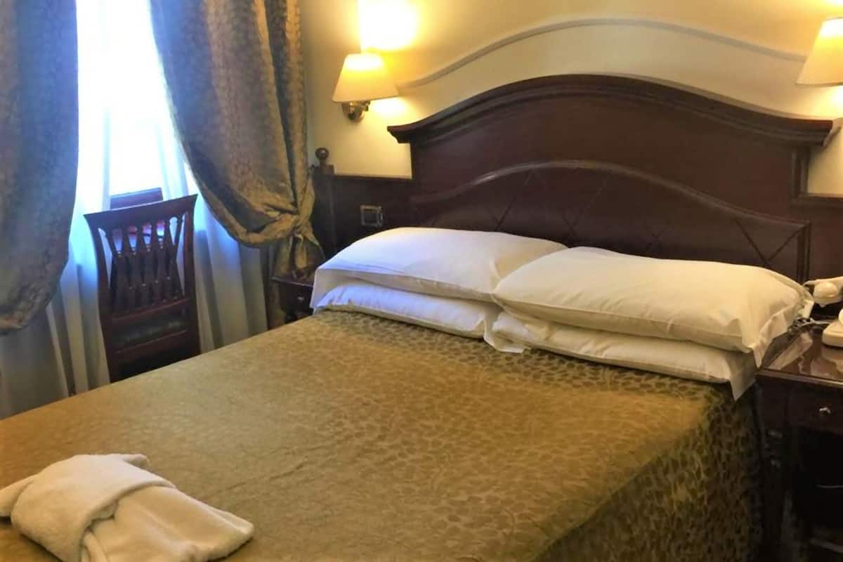 A neatly made bed with a patterned bedspread, two pillows, and a folded towel on the left side.
