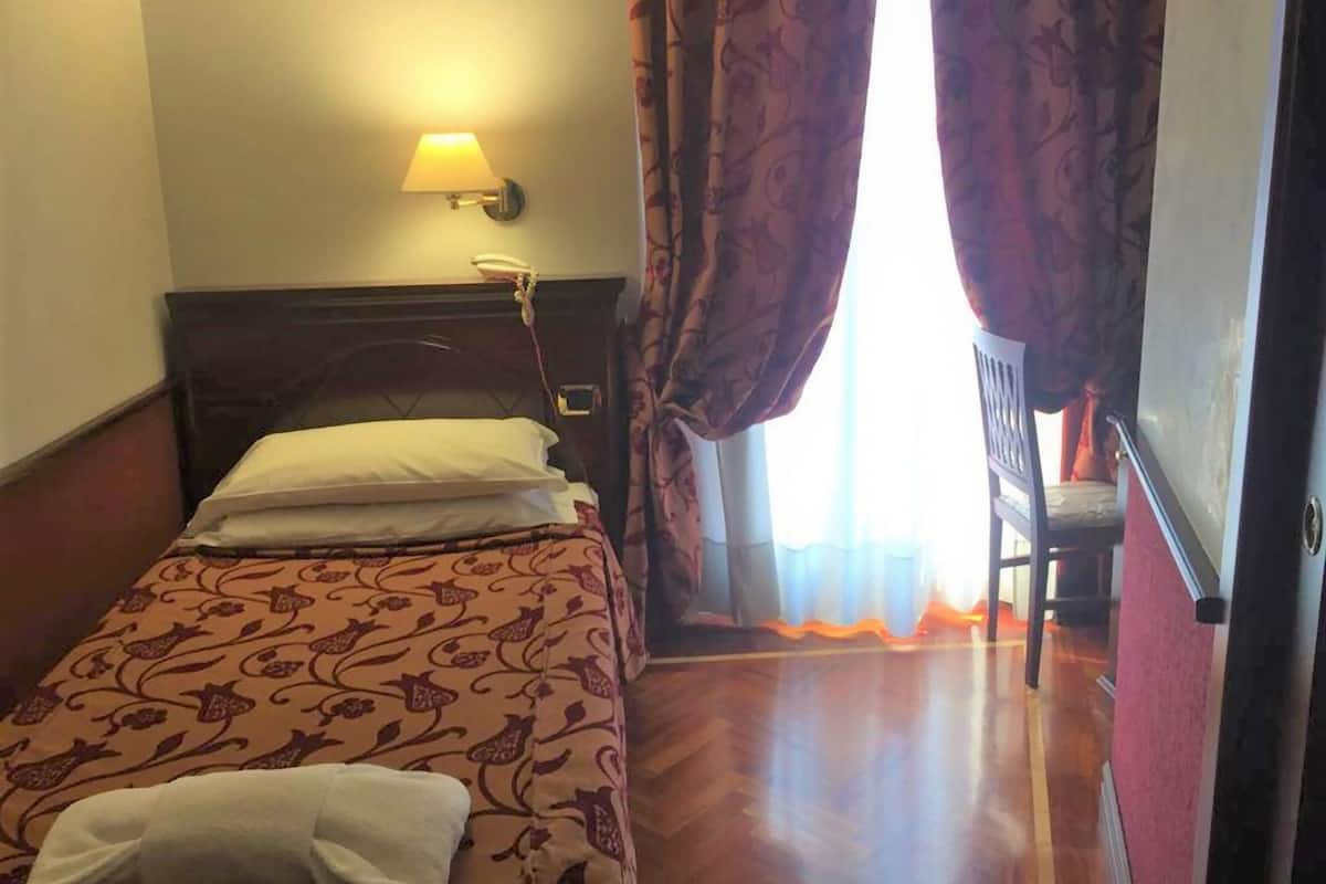 A hotel room with a bed, a nightstand, a lamp, and a chair near the window.