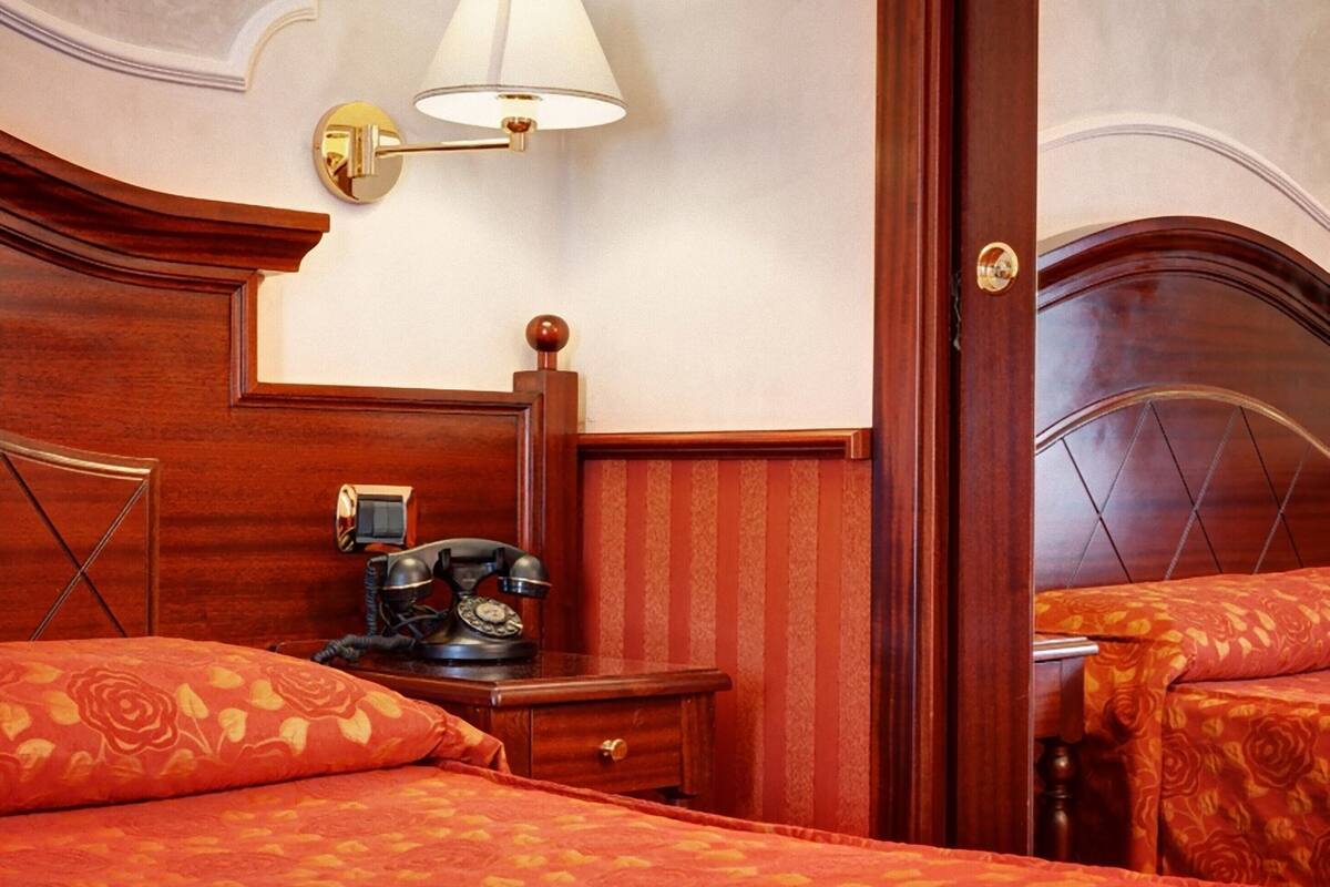 A hotel room with a wooden headboard, a bedside table with a telephone, and a lamp.