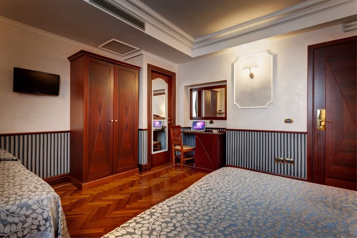 A hotel room with two beds, a desk with a computer, a TV, and a mirror.