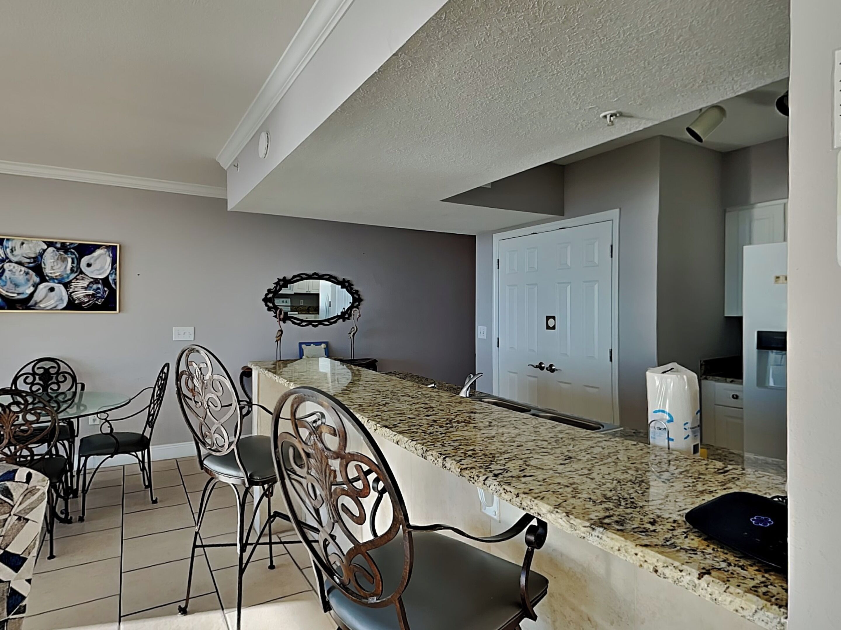 A dining area with a granite countertop, metal chairs, and a wall-mounted mirror.