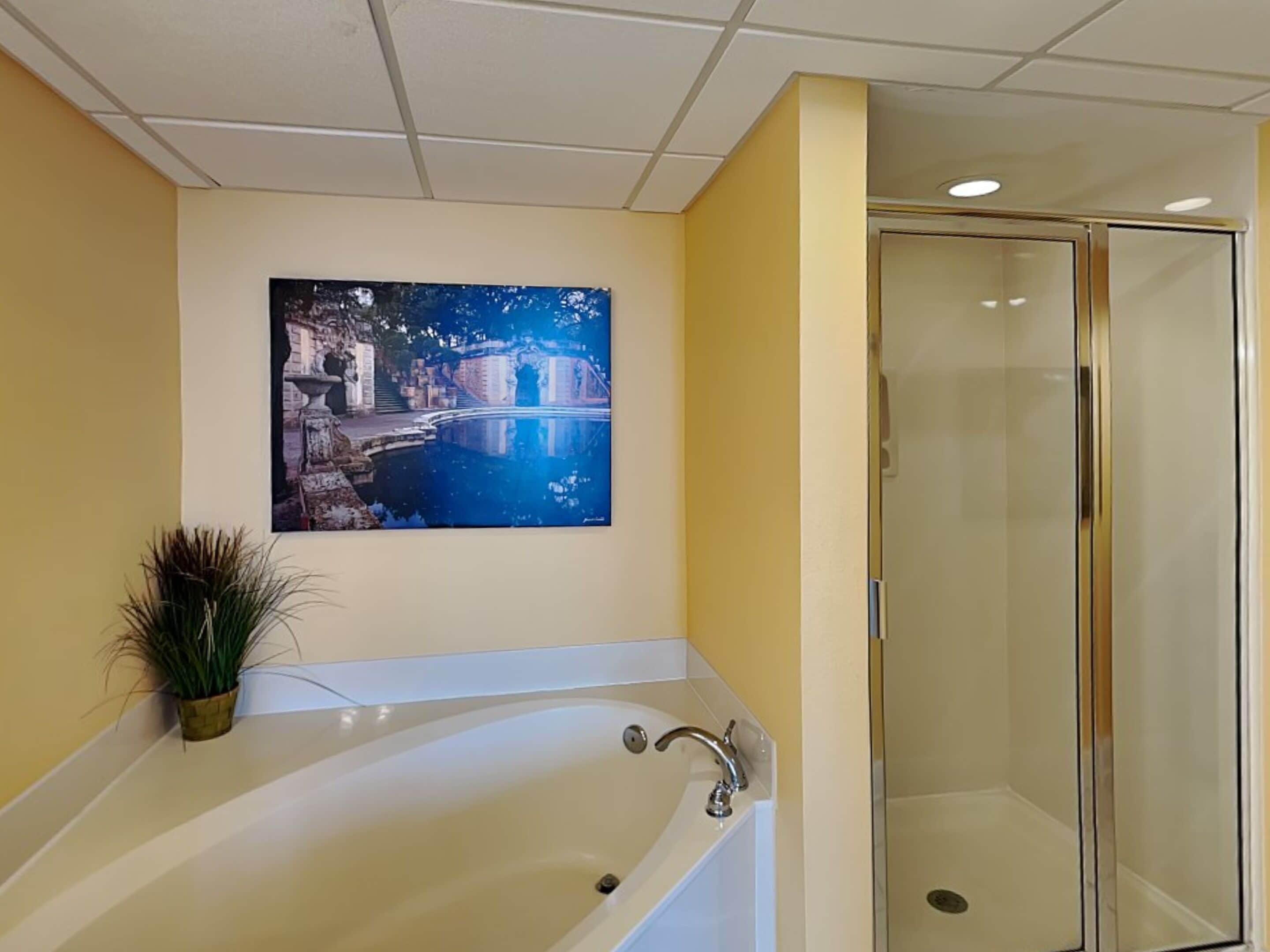 A bathroom with a bathtub, a glass shower enclosure, and a painting of a cityscape on the wall.
