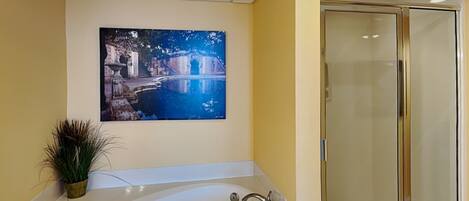 A bathroom with a bathtub, a glass shower enclosure, and a painting of a cityscape on the wall.