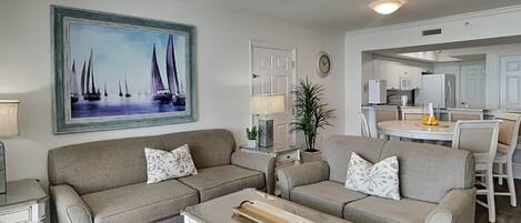 A living room with a sofa, coffee table, and a painting of sailboats.