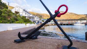 Escultura frente al agua con un ancla y un aro destacados, sobre un fondo de un edificio y una colina.