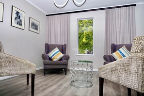 A modern living room with two patterned armchairs, a glass coffee table, and a large window with curtains.