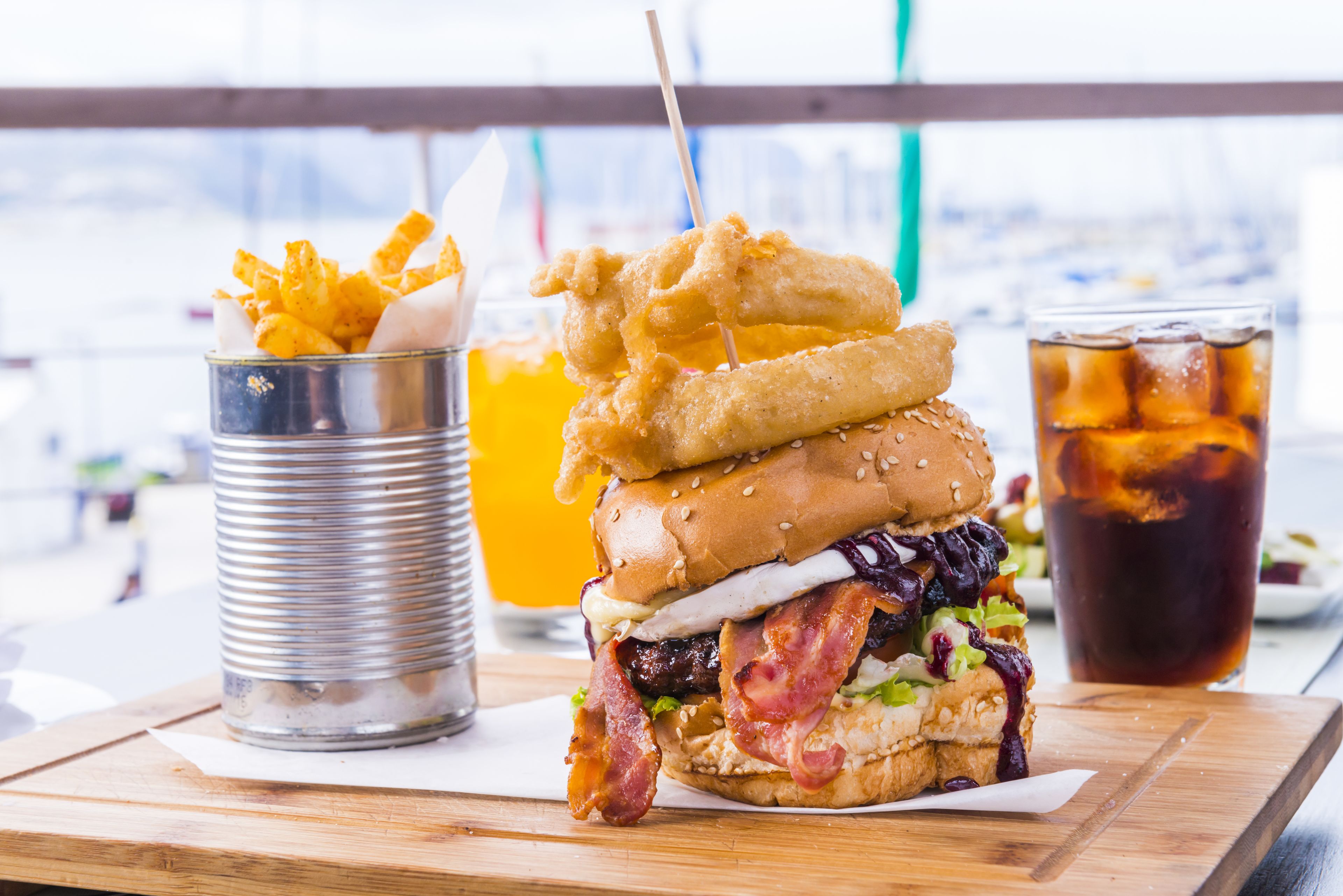 A burger with bacon, lettuce, and a sesame bun, accompanied by fries and a drink.