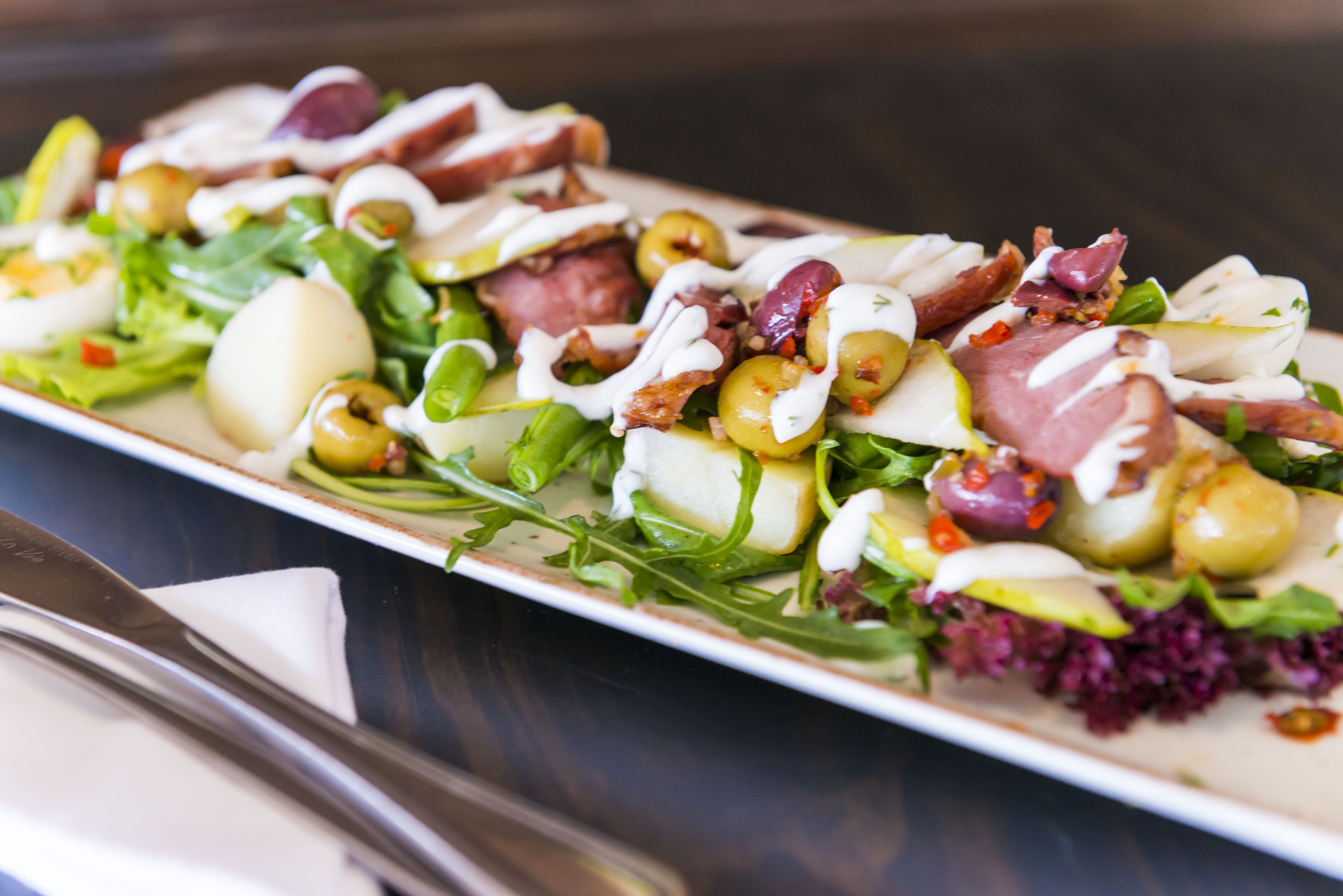 Un piatto impiattato con diversi ingredienti tra cui verdure, olive e carne, servito su un piatto rettangolare.