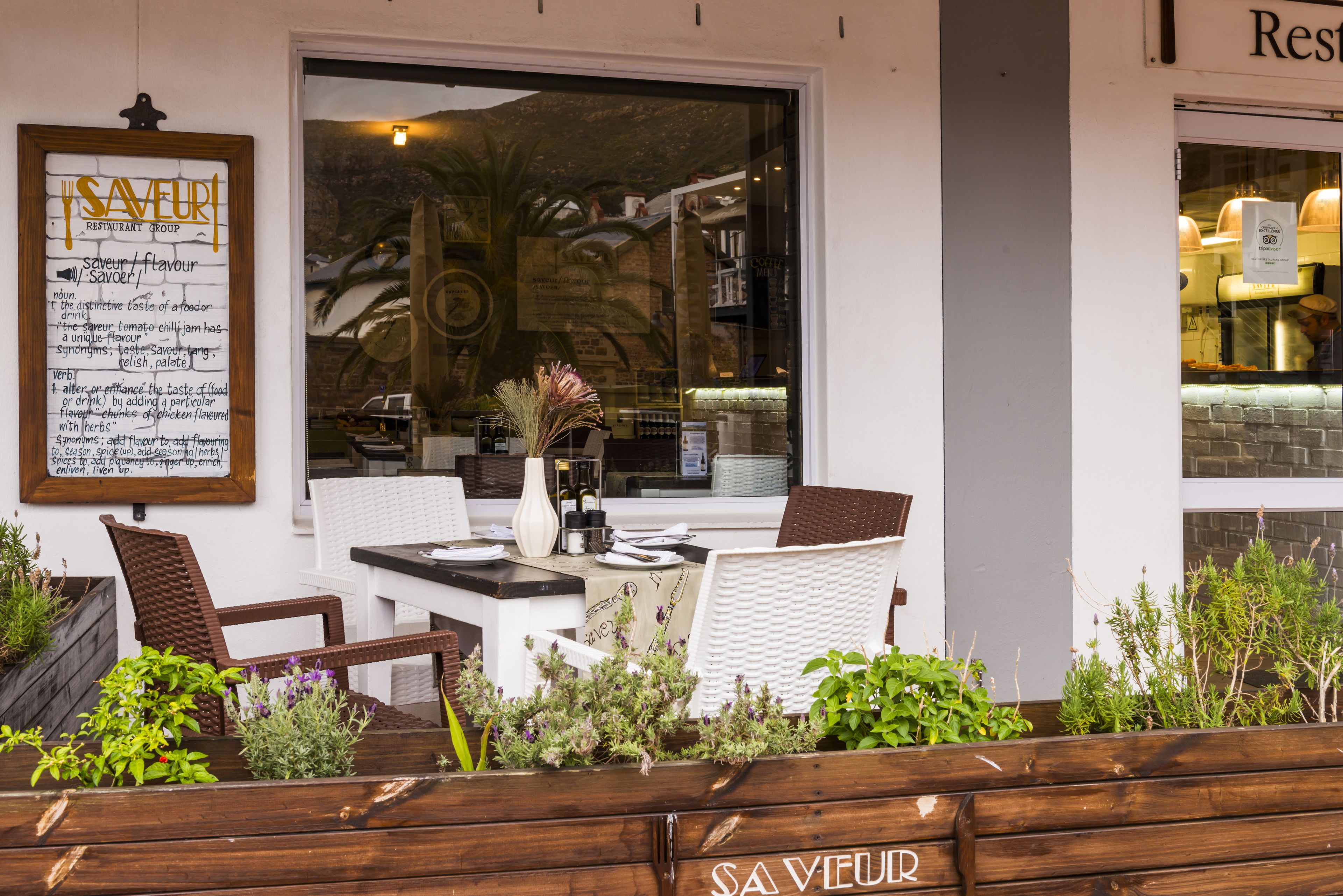Een terras met rieten meubels, een houten bank en een menubord.