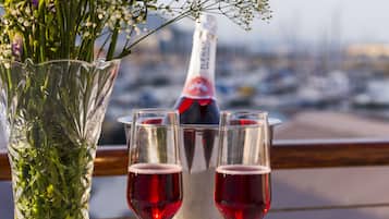 Una mesa con un florero de vidrio con flores moradas, dos copas de vino tinto, una botella de champán y una selección de bombones y fresas.