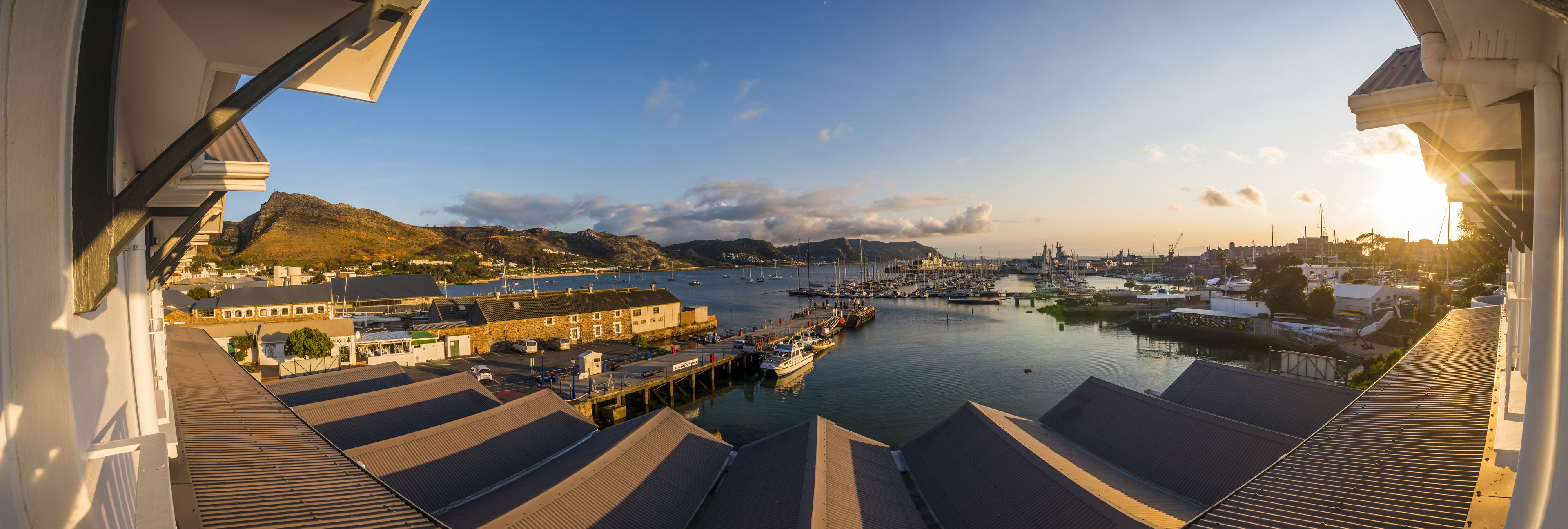 Vista panorámica de un puerto con barcos, edificios y montañas al fondo.