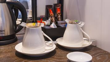 Duas cafeteiras brancas com pires, uma chávena branca e uma pequena tigela branca sobre uma mesa de madeira.
