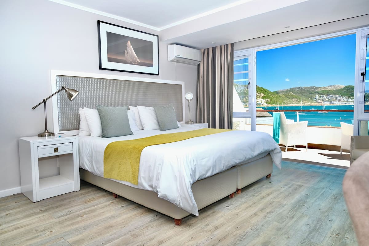 A modern hotel room with a large bed, a bedside table, a lamp, and a view of the sea.