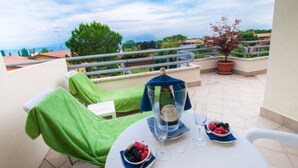 A balcony with a table set for two, a potted plant, and a view of the sea.
