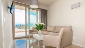 A modern living room with a beige sofa, a small table with a vase of flowers, and a view of the outdoors through a sliding glass door.