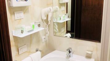 A bathroom with a white sink, two hair dryers, a mirror, and a towel rack.