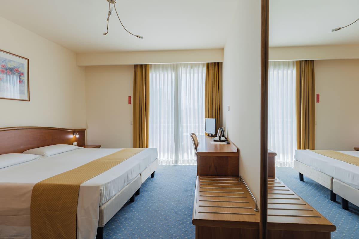 A hotel room with two beds, a desk, a chair, and a mirror.