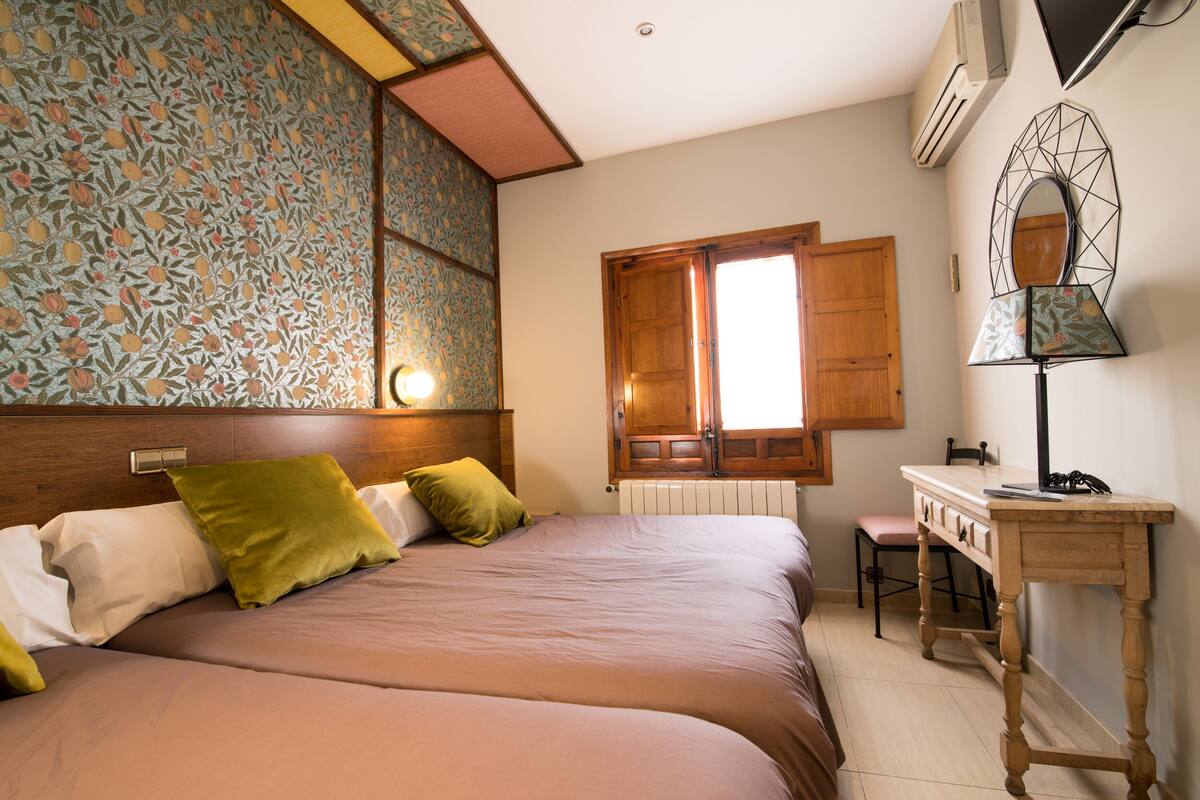 A bedroom with a bed, a wooden desk, a chair, a radiator, and a window with a wooden shutter.