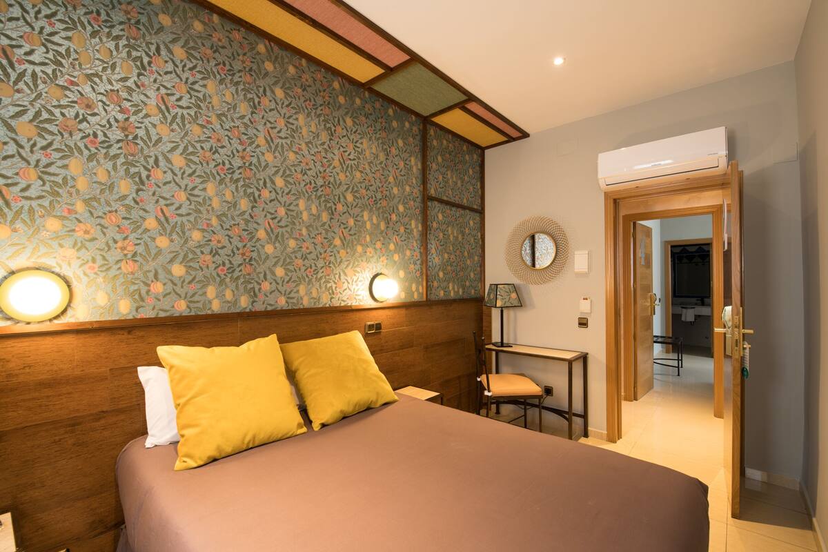 A hotel room with a bed, a nightstand, a lamp, and a door leading to a bathroom.