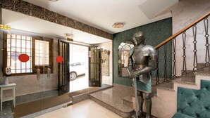 A lobby with a knight statue, a staircase, and a teal sofa. - Hotel Sol (Toledo)