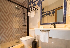 A modern bathroom with a glass shower enclosure, a white toilet, a sink with a mirror, and patterned tiles. - Hotel Sol (Toledo)