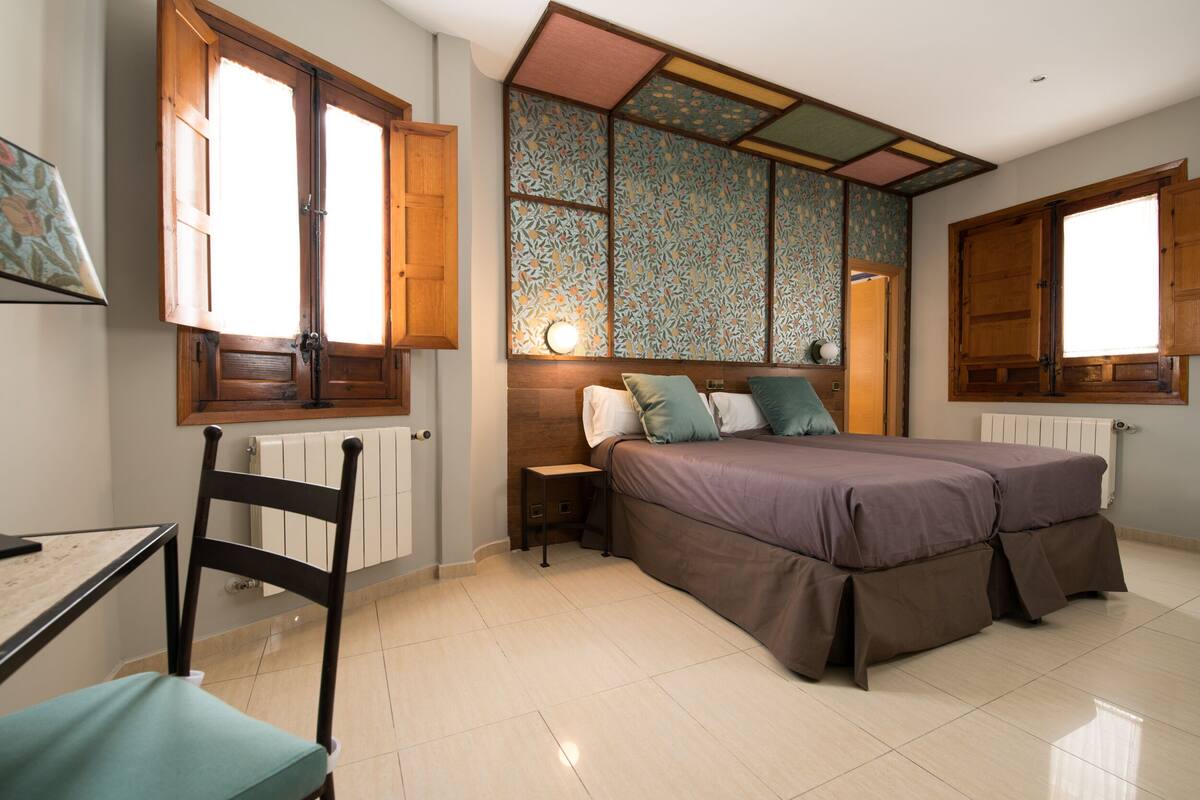 A bedroom with a bed, a chair, a nightstand, and a window with wooden shutters.