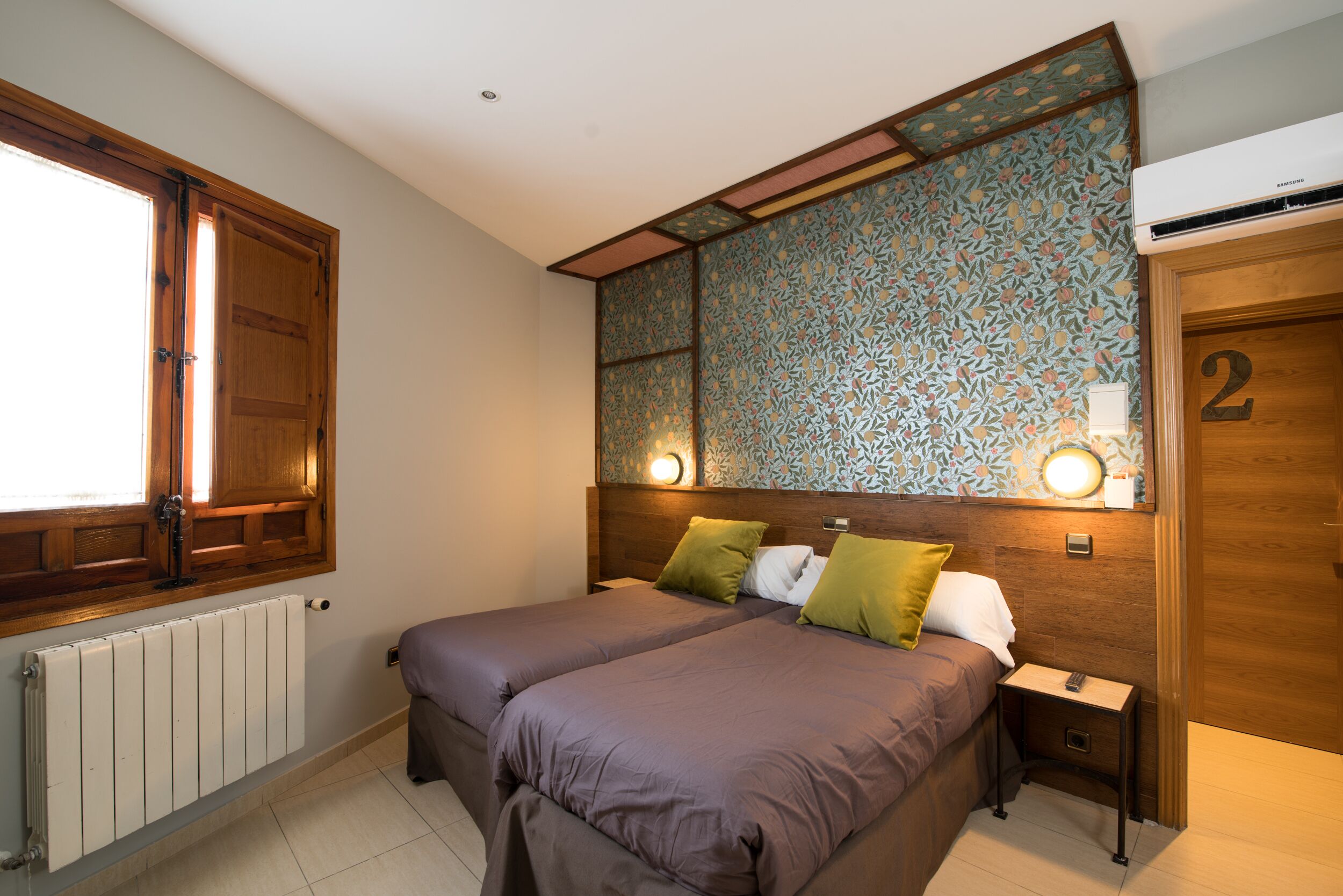 Ein Schlafzimmer mit zwei Betten, einem Heizkörper, einer Holztür mit der Nummer 2 und einer Wand mit Muster.