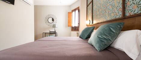 Une chambre à coucher comprenant un lit, des oreillers, un téléviseur fixé au mur, un climatiseur, une chaise, un miroir et une fenêtre donnant sur l’extérieur.