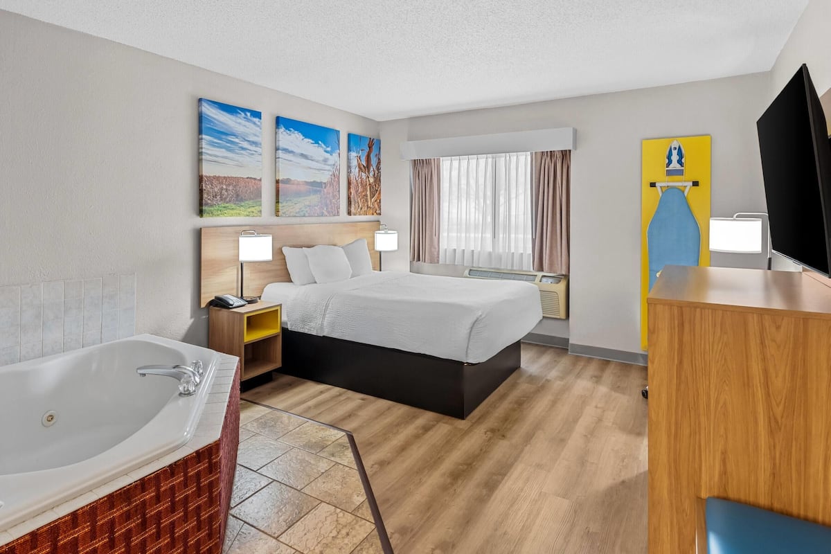 A hotel room with a large bed, a bathtub, a desk, and a television.