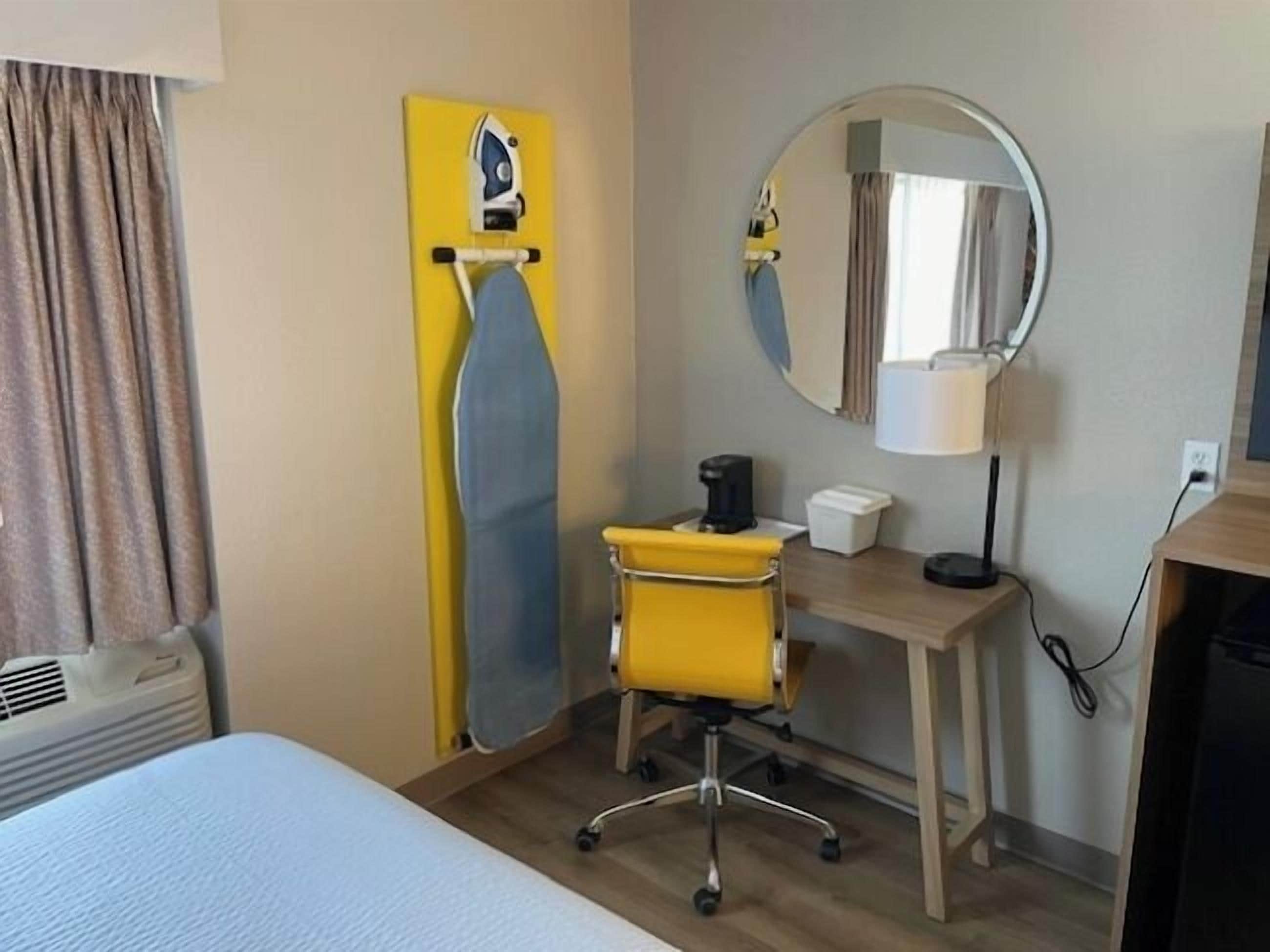 Habitació d'hotel amb llit, escriptori amb cadira, mirall, cafetera i taula petita.