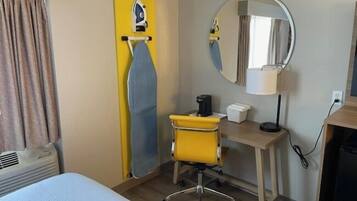 Habitació d'hotel amb llit, escriptori amb cadira, mirall, cafetera i taula petita.
