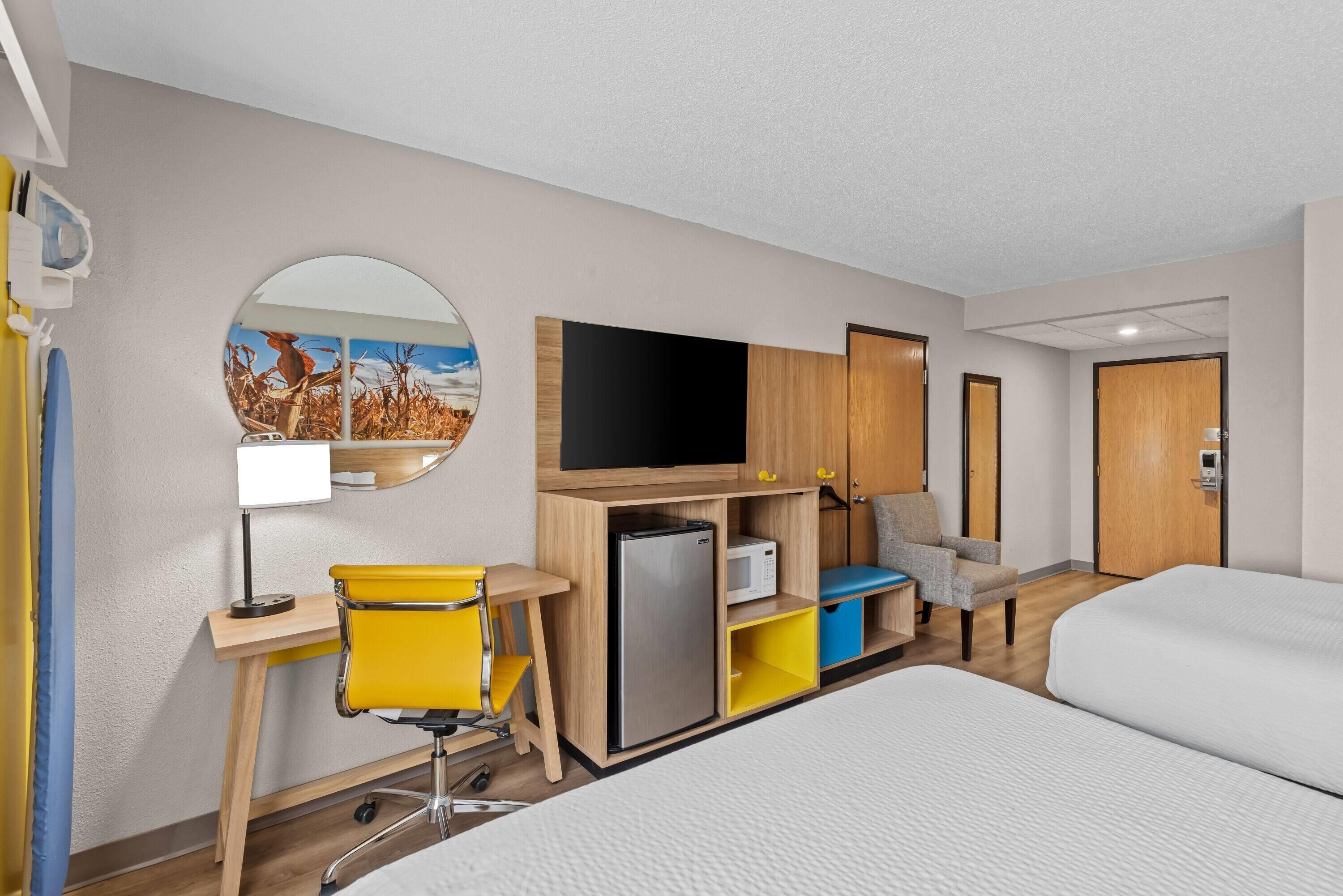 A hotel room with a bed, a desk with a chair, a television, a refrigerator, and a microwave.