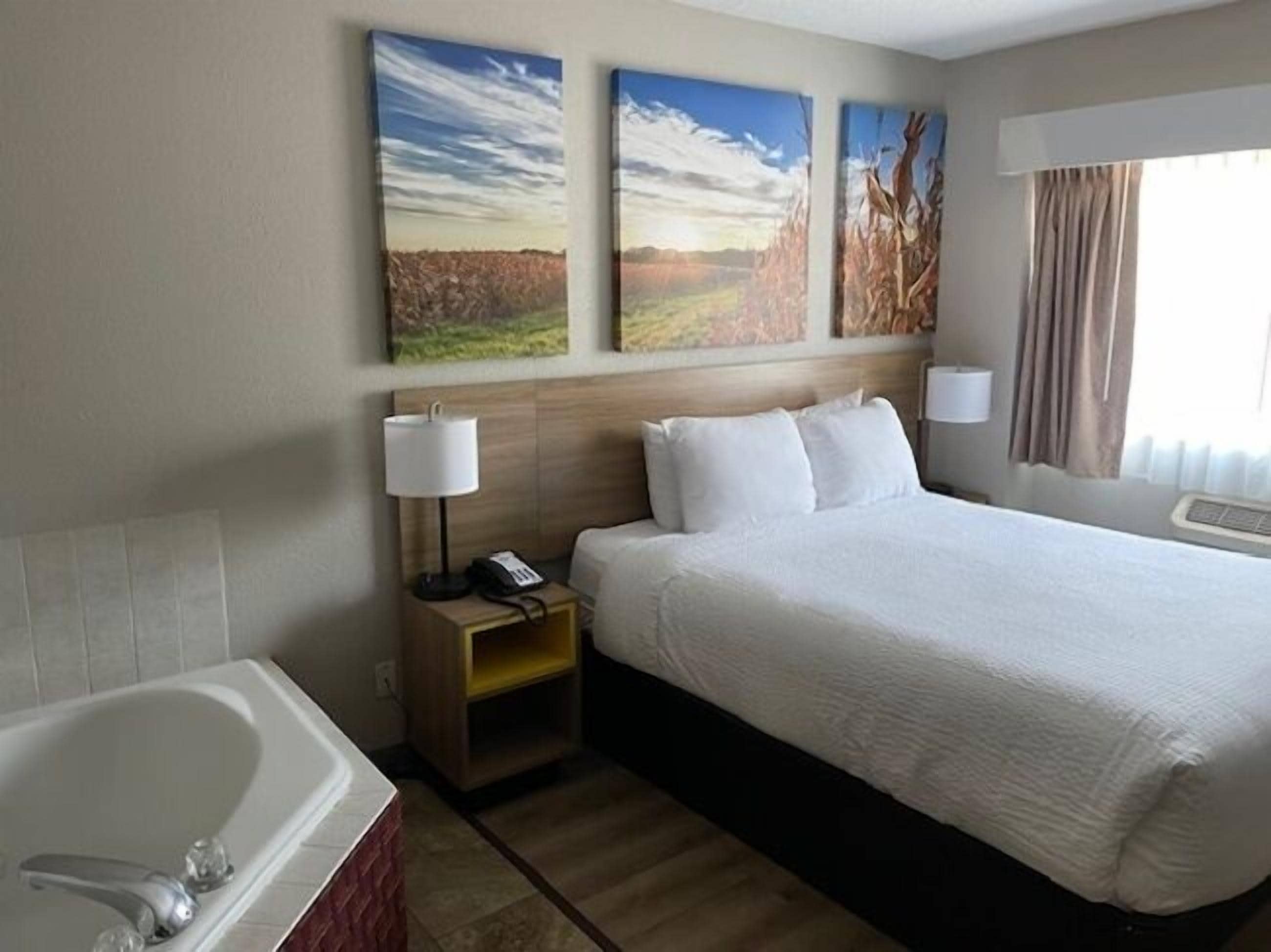 Une chambre d’hôtel avec un grand lit, une table de chevet avec une lampe, un téléphone et un tableau au mur.