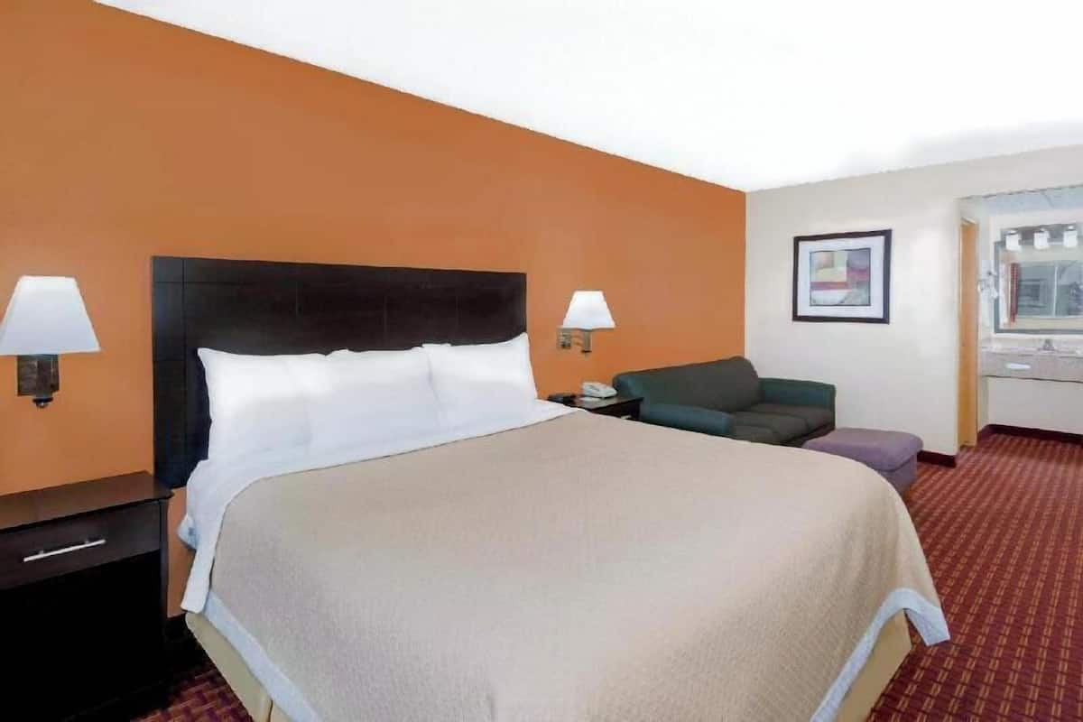 A hotel room with a large bed, two bedside lamps, a sofa, a small table, and a window.