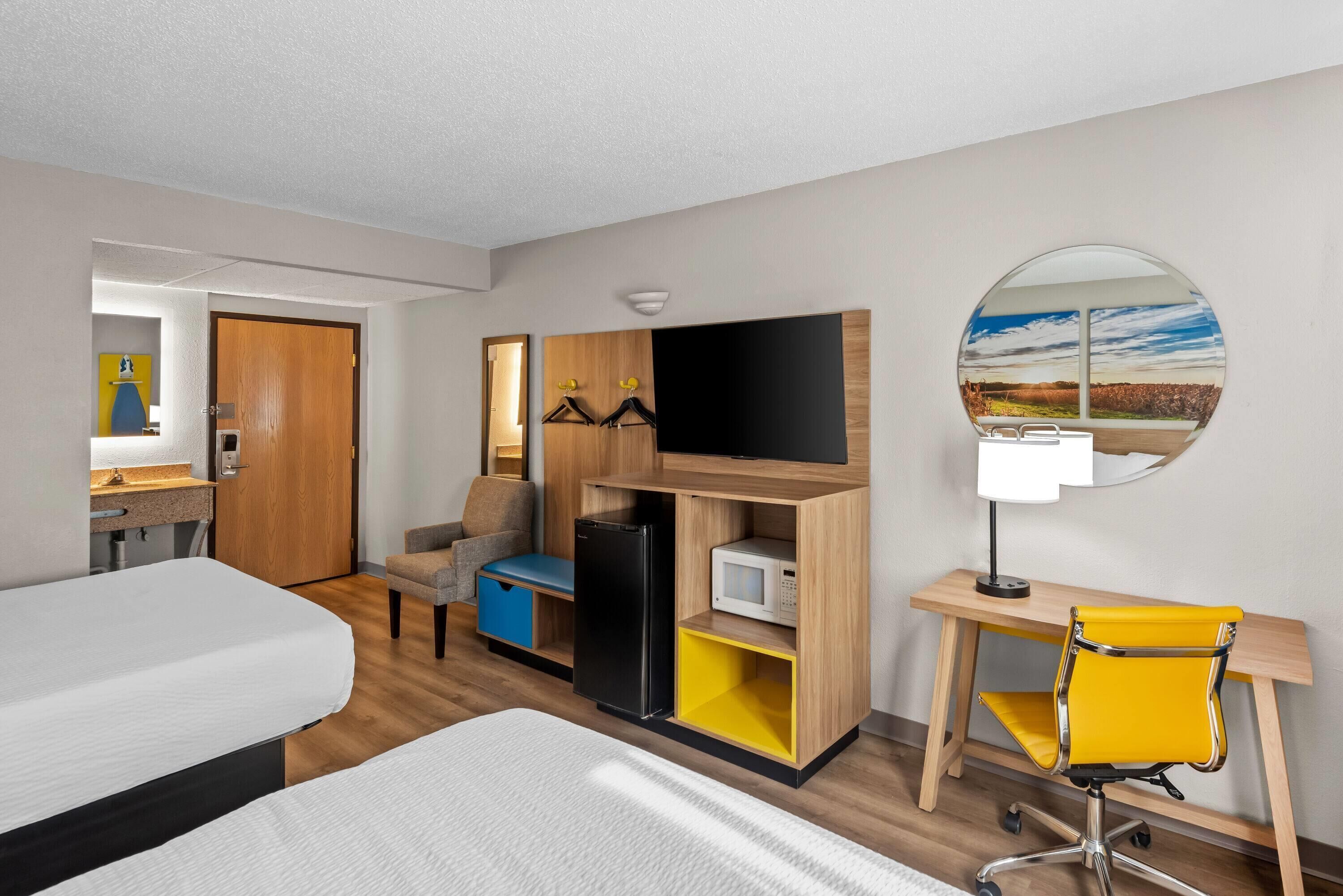 Een hotelkamer met een bed, een bureau met stoel, een televisie, een spiegel en een kledingkast.