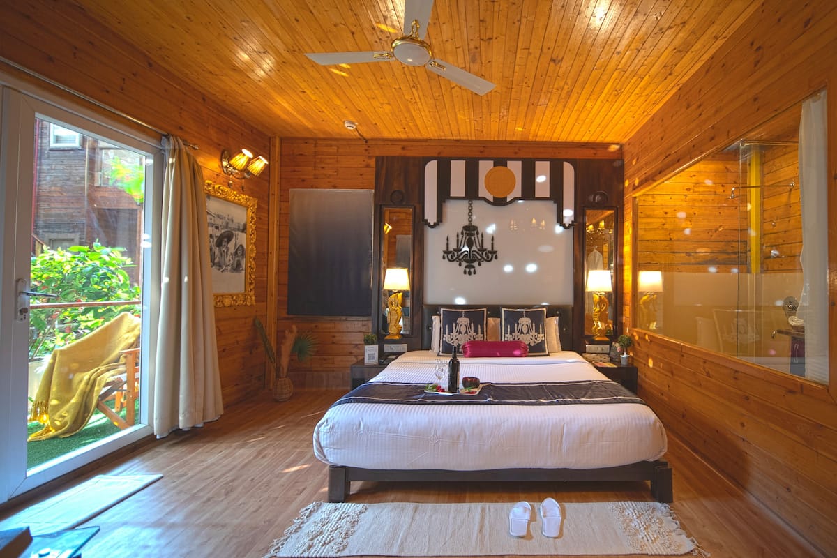 A wooden cabin bedroom with a bed, a chandelier, and a large window.