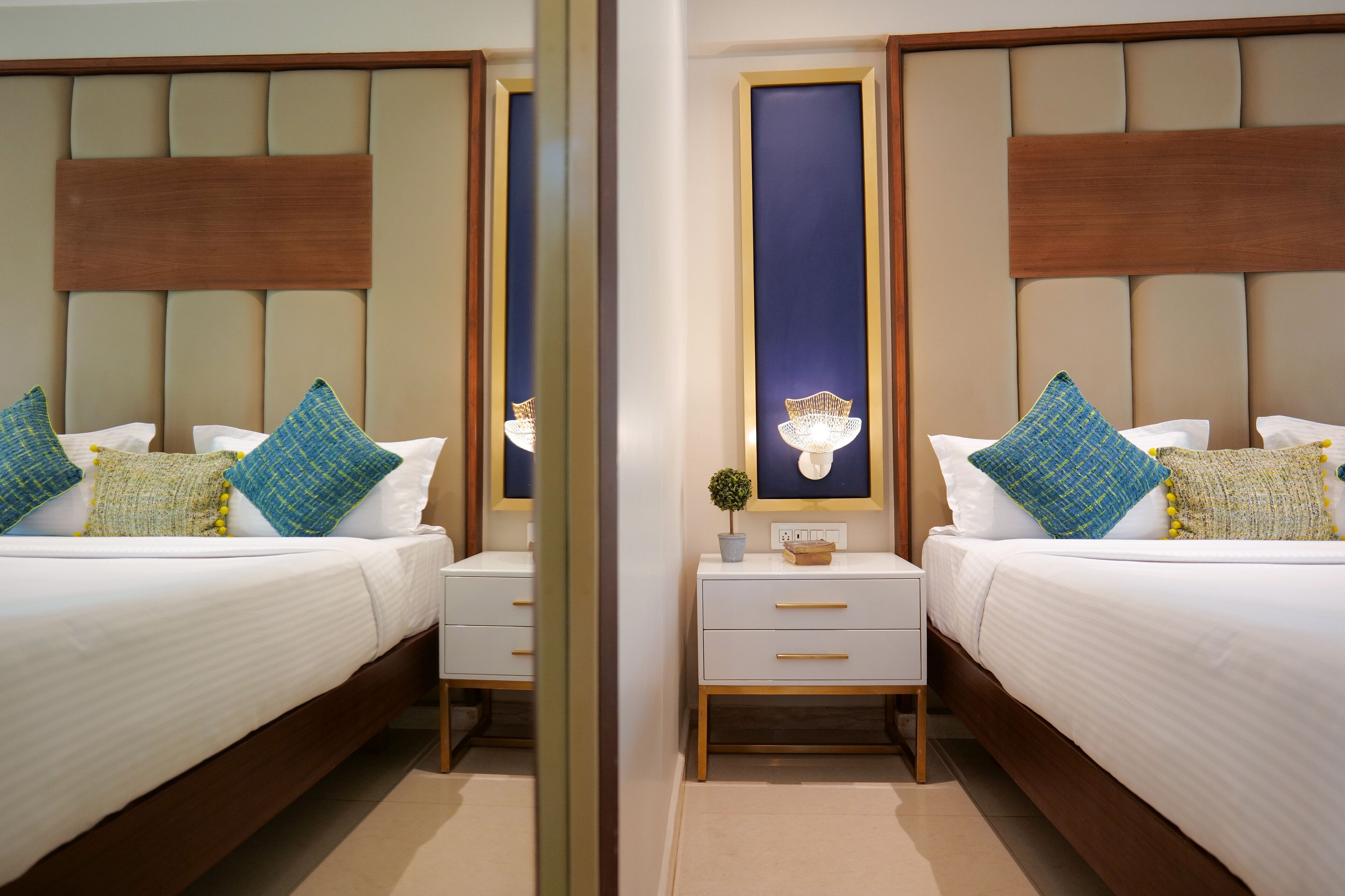 A mirrored view of a hotel room with two beds, nightstands, and a wall-mounted lamp.