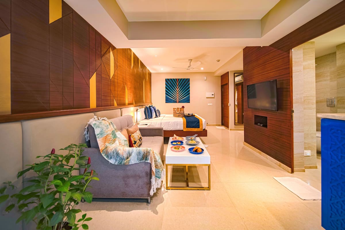 A modern hotel room with a sofa, a bed, a TV, and a small dining table with food.