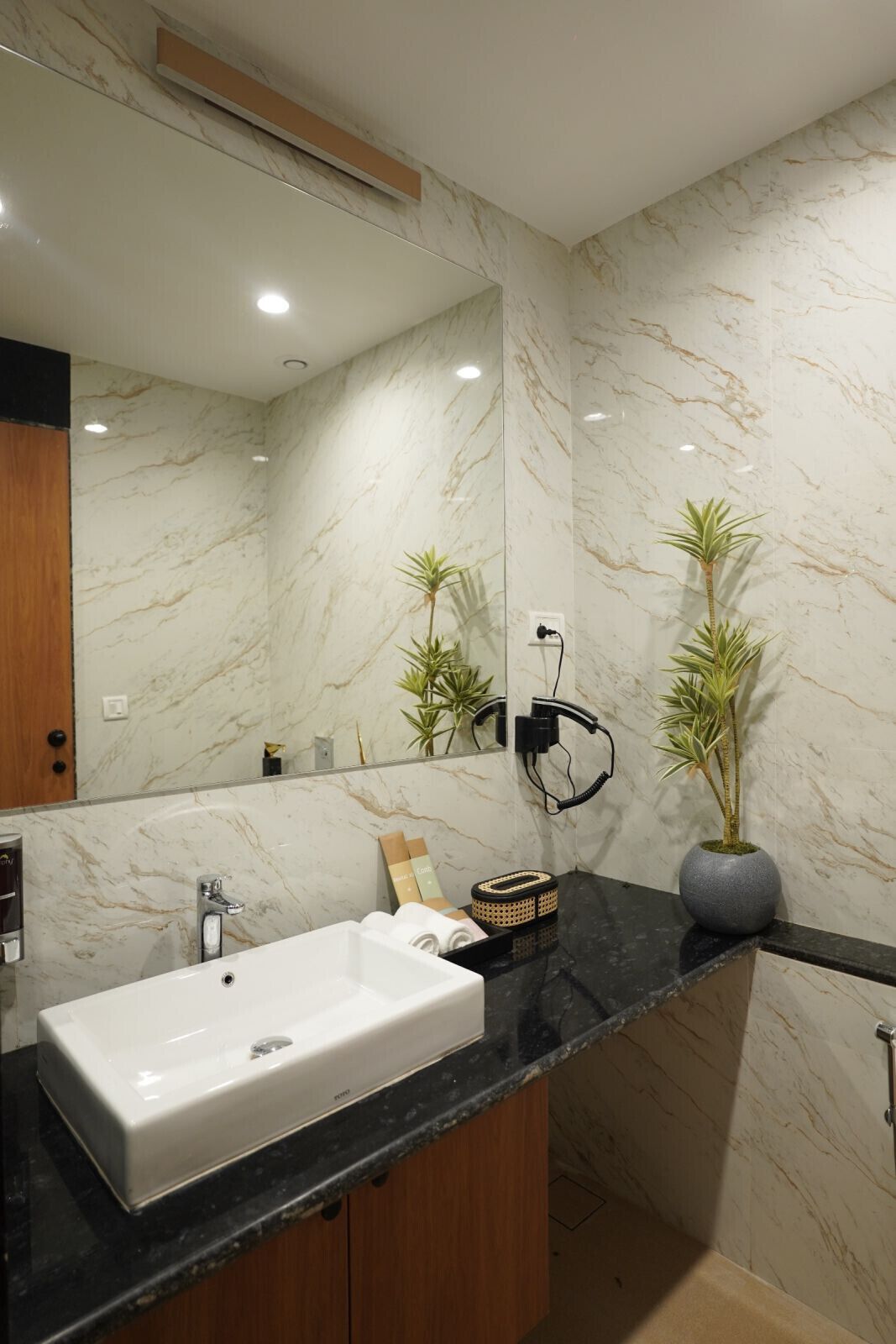Un baño moderno con pared de mármol, encimera negra, lavabo blanco y espejo.