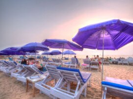 A beach with rows of sun loungers and purple umbrellas.