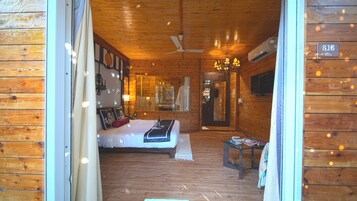 A wooden cabin interior with a bed, a ceiling fan, a chandelier, and a mirror.