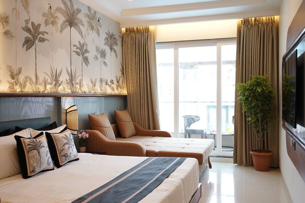 A hotel room with two beds, a large window with curtains, a potted plant, and a wall-mounted TV.