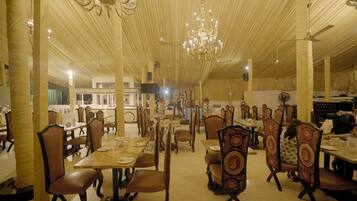 A spacious dining area with high ceilings, chandeliers, and ornate chairs. Tables are set with plates and glasses.