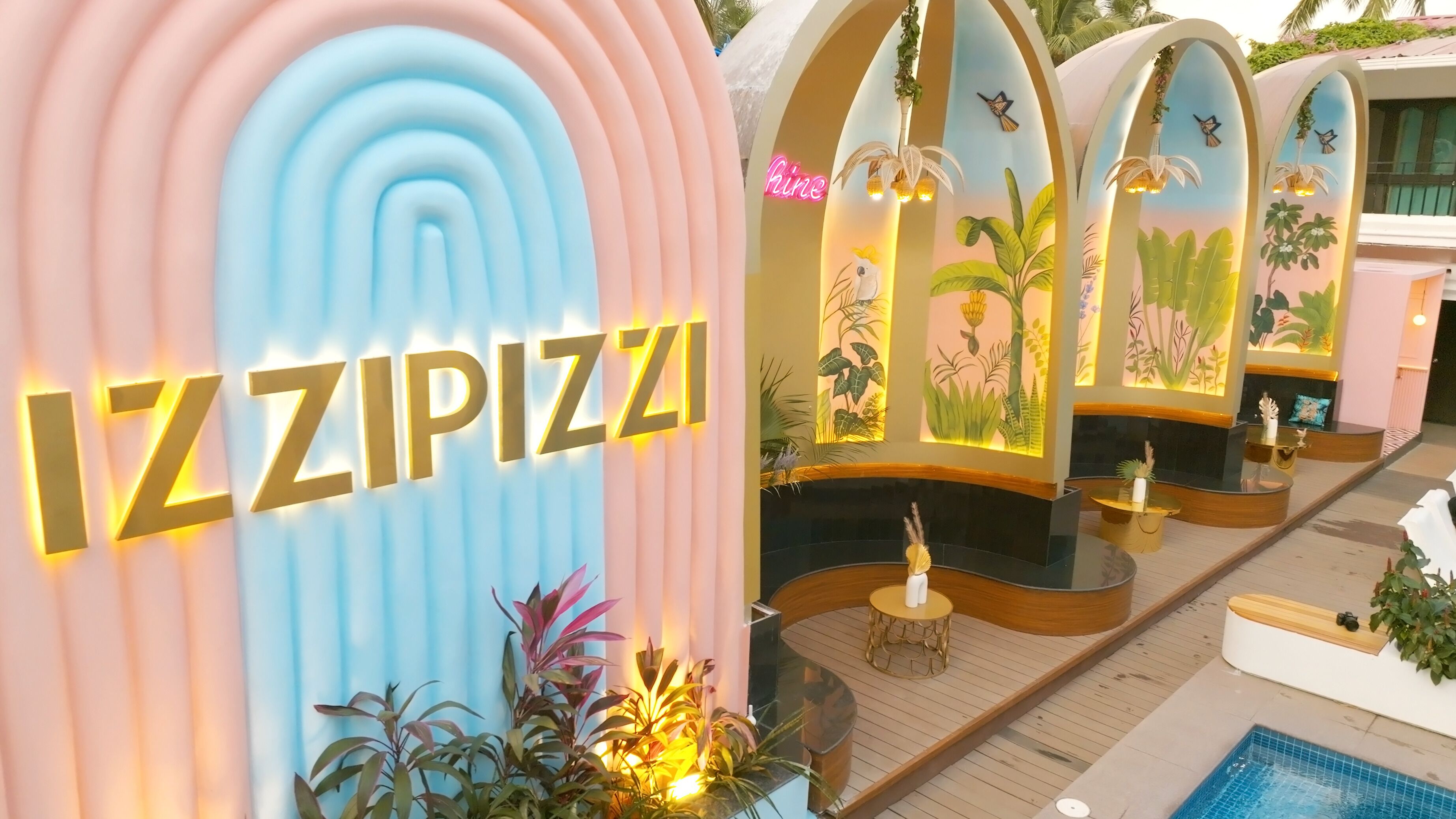 A hotel lobby with a large illuminated sign reading "IZZIPIZZI," a reception desk, and a pool area.