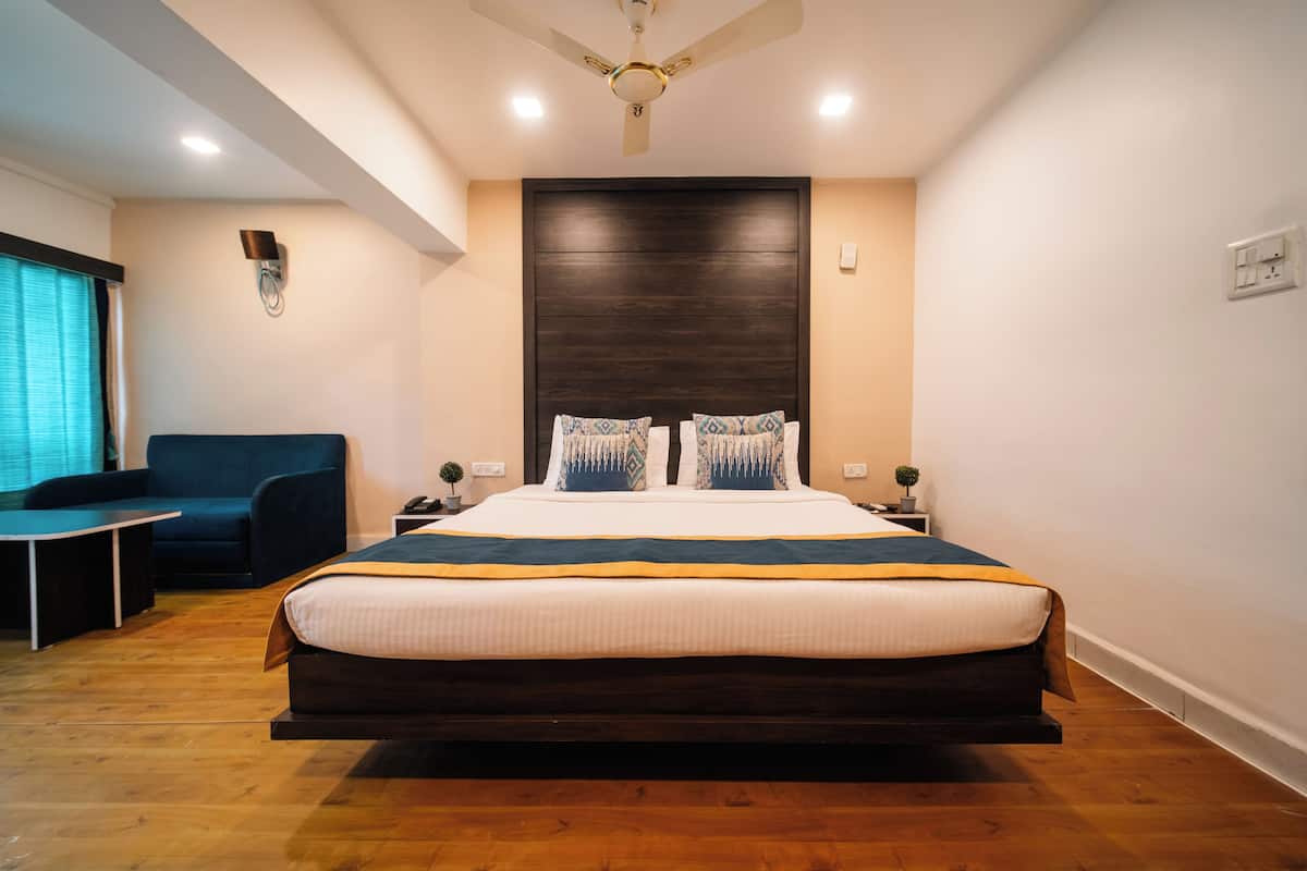 A modern bedroom with a large bed, dark headboard, bedside tables, and a small desk with a chair.