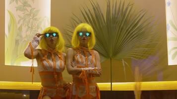 Two individuals in matching outfits standing in front of a neon sign that reads "Goodtimes".