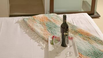 A hotel room with a bed, a glass shower enclosure, a white bathtub, and a tray with a bottle and glasses on the bed.