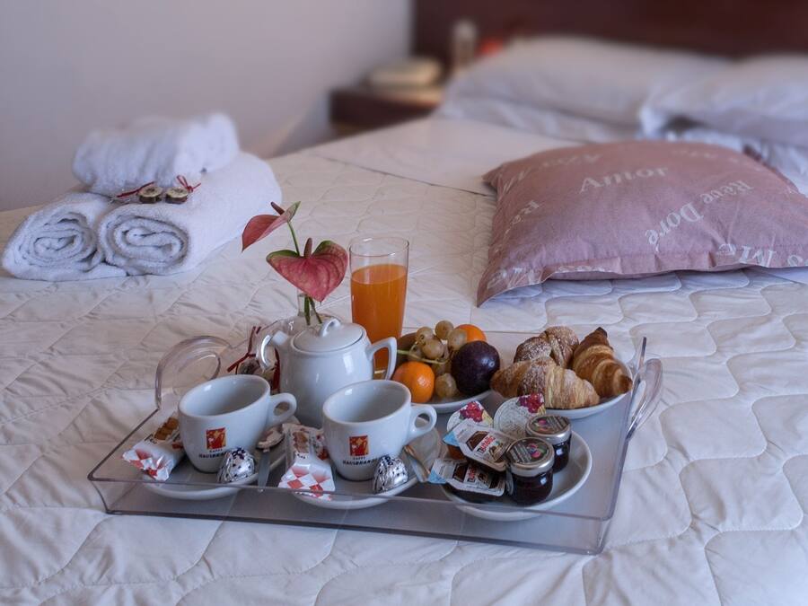 A neatly made bed with a tray of breakfast items including croissants, fruits, and a glass of orange juice.